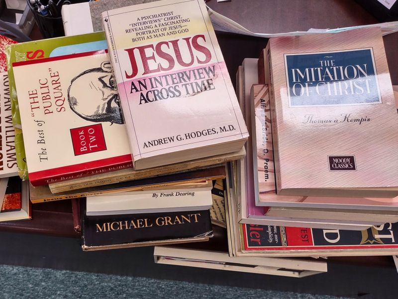 A stack of various books including titles on religion, philosophy, and history, sitting on a wooden surface, in a disorganized arrangement.